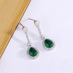 Macro detail of drop earrings with green pear-shaped gemstones and zircon halo setting
