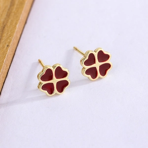 Dettaglio ravvicinato di orecchini a quadrifoglio dorati con petali a cuore in smalto rosso