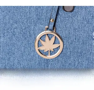 Detailed close-up of a golden hollow maple leaf metal pendant on a blue denim tote bag