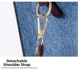 Detail of detachable gold hook on blue denim tote with heavy-duty leather strap connection