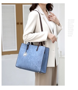 Detail of blue denim tote bag featuring premium brown leather straps and metallic leaf charm
