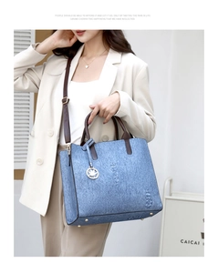 Blue denim tote bag with brown straps and maple leaf charm shown on a model
