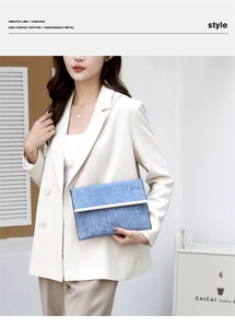 Detail of blue denim textured envelope bag with gold metal trim and chain strap