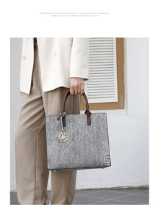 Close-up of gray textured tote bag with brown handles and a gold maple leaf charm detail
