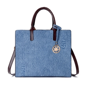 Blue denim tote bag with distressed details and brown leather handles on white background