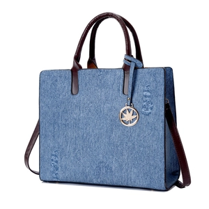 Denim blue large tote bag with brown leather handles and a maple leaf metal pendant