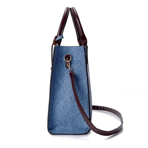 Blue denim tote bag with brown leather handles and adjustable shoulder strap shown in side view