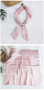 Close-up of a pink silk scarf featuring white floral patterns and paisley borders