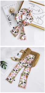 Detailed view of floral silk scarf styled on an art magazine and a woven summer straw bag