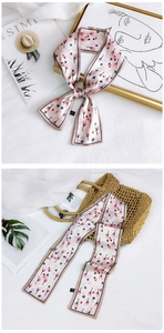 Detailed view of pink floral twilly scarf tied on a woven bag and styled with magazines