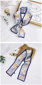 Close-up of a floral skinny silk scarf with blue borders on a minimalist art background