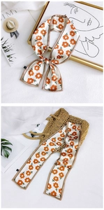 Detail of floral skinny scarf tied on a straw bag with orange flower patterns