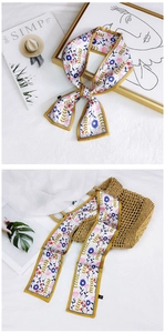 Floral skinny silk scarf tied on a straw bag with yellow borders and blue flower patterns