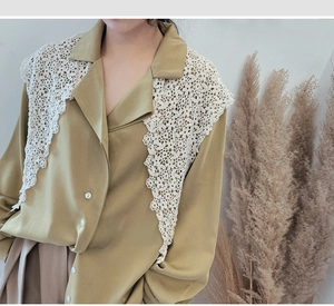 Detailed close-up of a vintage mustard yellow shirt with an intricate white lace shawl collar