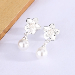Macro shot of silver flower stud earrings with elegant white pearl drops on white surface