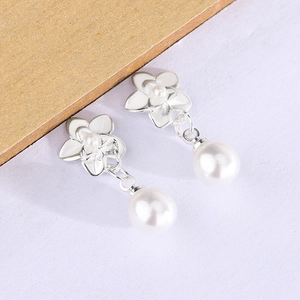 Macro view of silver flower earrings with hanging round white pearls on a soft background