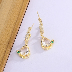 Detail of gold drop earrings with zircon crystals and a green gem on purple background