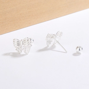 Silver bow-shaped threaded stud earrings with a hollow mesh design on a wooden background