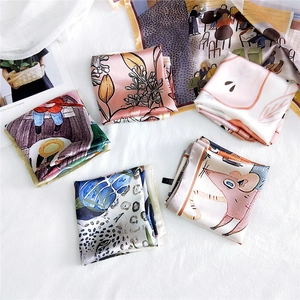 Flat lay of diverse floral and leopard print silk square scarves on a white fabric surface