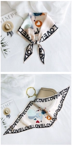 Detail view of beige silk scarf with cartoon heart patterns and LOVE text print on a bag