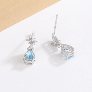 Macro detail of silver drop earrings with star studs and pear-cut light blue zircon stones