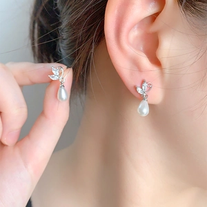 Detailed close-up of a silver butterfly wing earring with a drop pearl on the ear