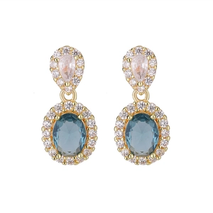Dettaglio degli orecchini a goccia dorati con zircone rosa e gemma ovale blu incastonata