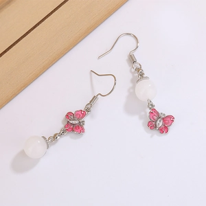 Détail de boucles d'oreilles papillon roses avec perles blanches sur fond en bois