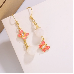 Détail de boucles d'oreilles papillon avec placage en or, émail rose et perles blanches