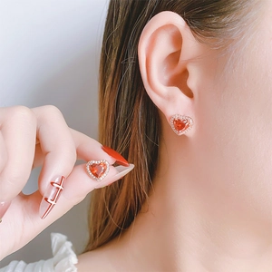 Detailed view of heart-shaped earrings with red zircon and rose gold setting on ear