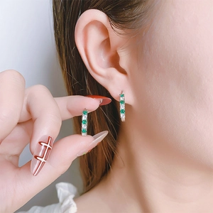 Detailed view of silver huggie earrings featuring alternating green and white zircons
