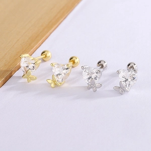 Macro detail of heart-shaped zircon and butterfly screw back earrings in gold and silver