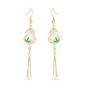 Detailed close-up of gold tassel earrings featuring white gourd charms and white pearls