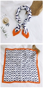Close-up of silk scarf with navy blue waves and orange border on white linen