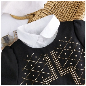 Détail du chemisier noir avec col Peter Pan blanc et motif de losanges dorés cloutés