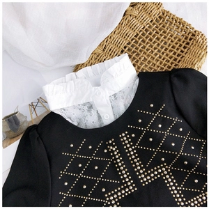 Détail d'un col en dentelle blanche sur chemisier noir orné de perles métalliques chic