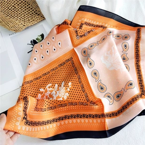 Elegant orange and peach paisley satin square scarf styled with resort lifestyle props