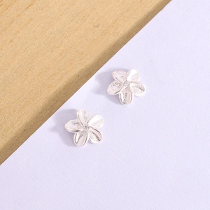 Macro shot of silver floral stud earrings with frosted metal texture and center zircon