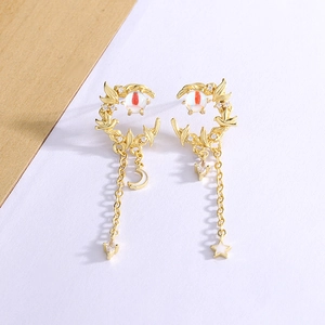 Detail of asymmetric gold moon tassel earrings with bird motifs and red cat eye stone