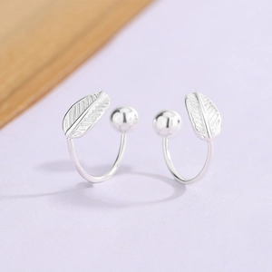 Macro detail of silver feather earrings with leaf texture and polished beads on purple base