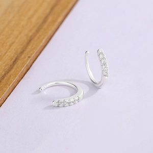 Close-up of silver C-shaped ear cuffs featuring micro-set white zircon stones on purple background