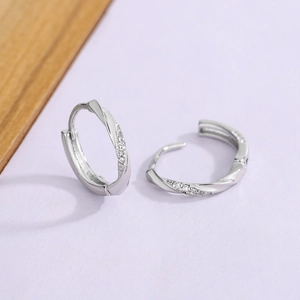 Elegant silver twisted button earrings with sparkling cubic zirconia on purple background
