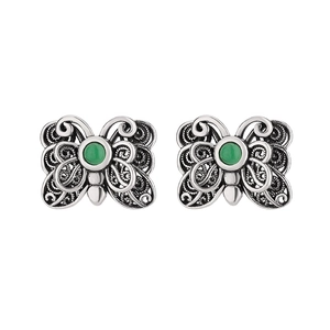 Macro shot of silver butterfly earrings with intricate filigree and green gemstone inlay