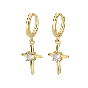 Détail de boucles d'oreilles dorées en croix avec zircon brillant serti au centre de l'étoile