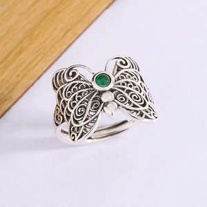 Macro detail of silver butterfly ring with green gemstone and hollow filigree pattern