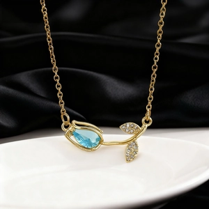 Elegant gold tulip necklace featuring a blue gemstone bud and sparkling pavé diamond leaves