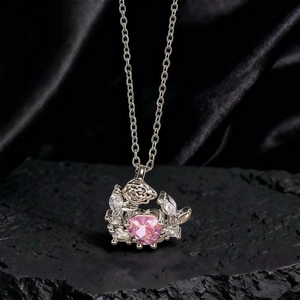 Detalle macro del collar plateado con gema de corazón rosa sobre seda negra y roca volcánica