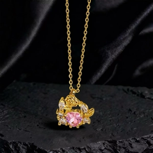 Detalle de collar dorado con colgante de corazón de circón rosa y motivos de rosa y hoja