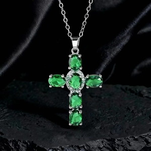 Dettaglio ravvicinato della collana a croce in argento con gemme verdi su roccia nera