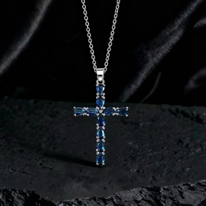 Dettaglio macro di un ciondolo a croce in argento con pietre blu e zirconi scintillanti